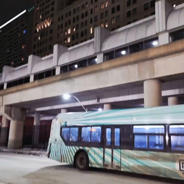 Wrapped DDOT bus parked beneath the People Mover tracks at night with snow on the ground