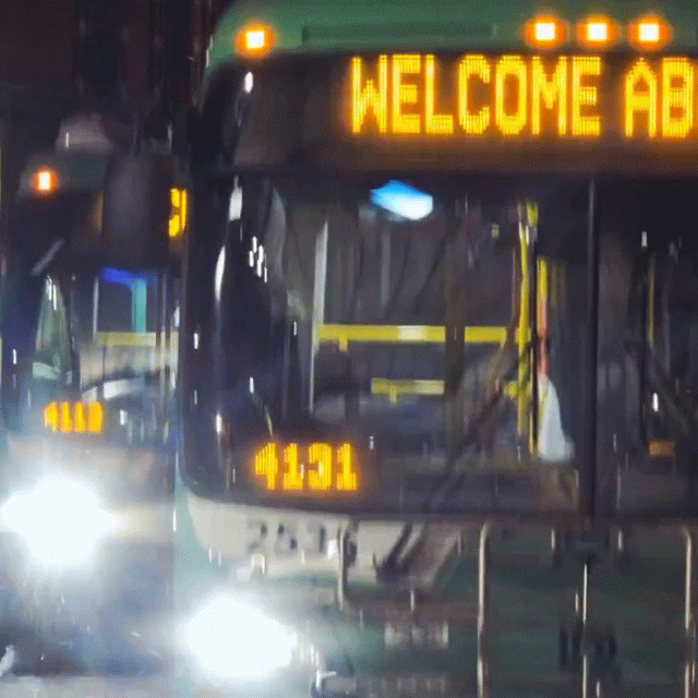 Two DDOT buses nose to nose at night with a lit Welcome Aboard display